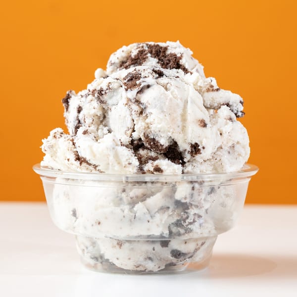 A clear cup filled with cookies and cream ice cream against an orange background.