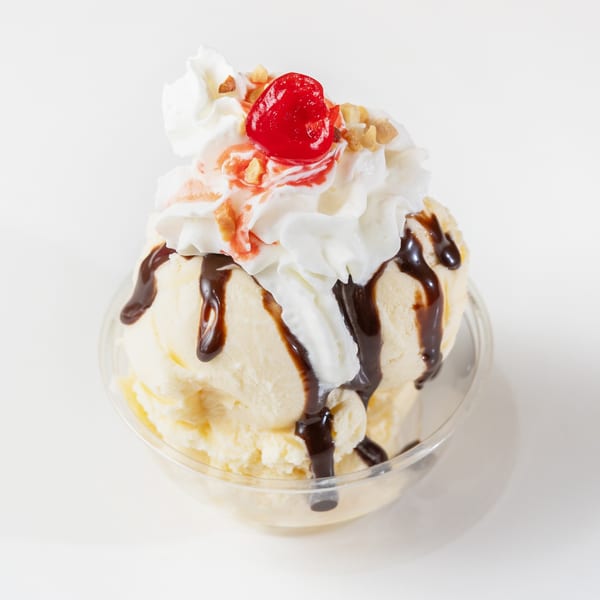 Vanilla ice cream sundae with chocolate syrup, whipped cream, cherry, and nuts in a clear cup.