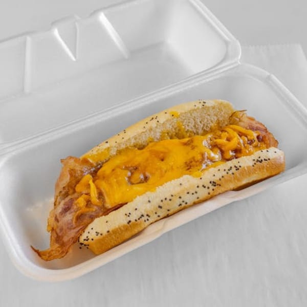 A chili cheese dog with bacon in a white styrofoam container from Unbeatable Eatables Inc.