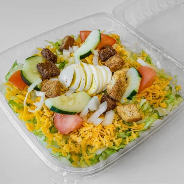 A fresh garden salad with lettuce, shredded cheese, tomatoes, cucumbers, onions, croutons, and sliced hard-boiled egg in a clear plastic container.