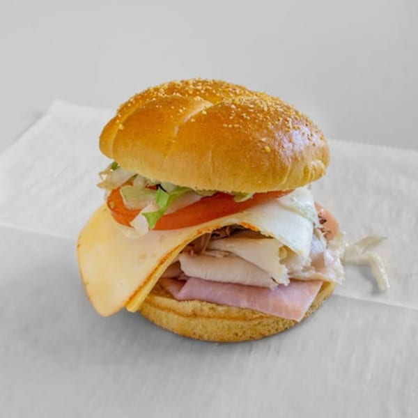 A deli sandwich from Unbeatable Eatables Inc. with ham, turkey, cheese, lettuce, and tomato on a bun.