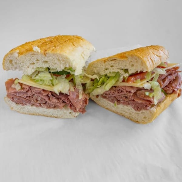 Two halves of a large Unbeatable Eatables sandwich with meat, cheese, lettuce, and tomatoes.